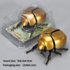 A golden wind-up insect toy, resembling a ladybug or bee, is shown inside its clear plastic packaging.