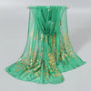 A sheer emerald green chiffon scarf with gold shimmer embroidery displayed on a hanger.