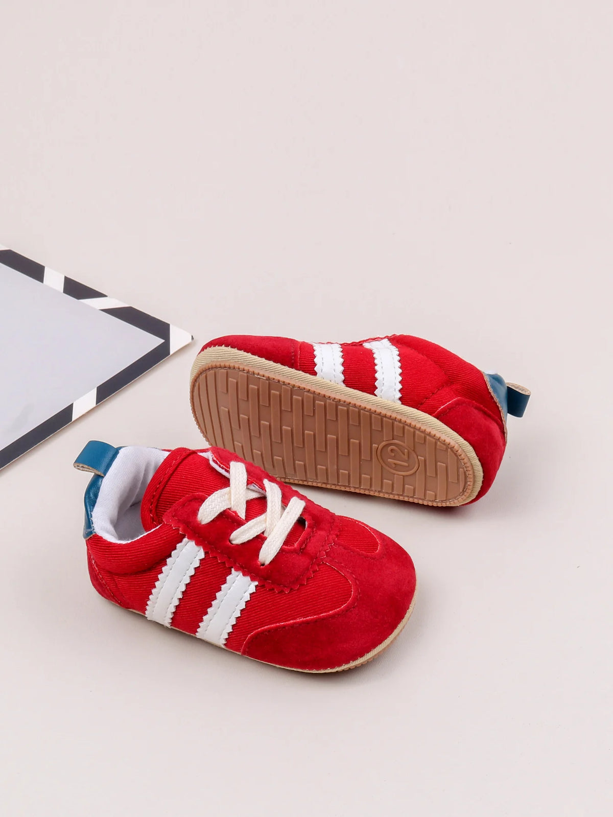A pair of red and white Adidas baby first walker shoes with a brown anti-slip sole resting on a light background.