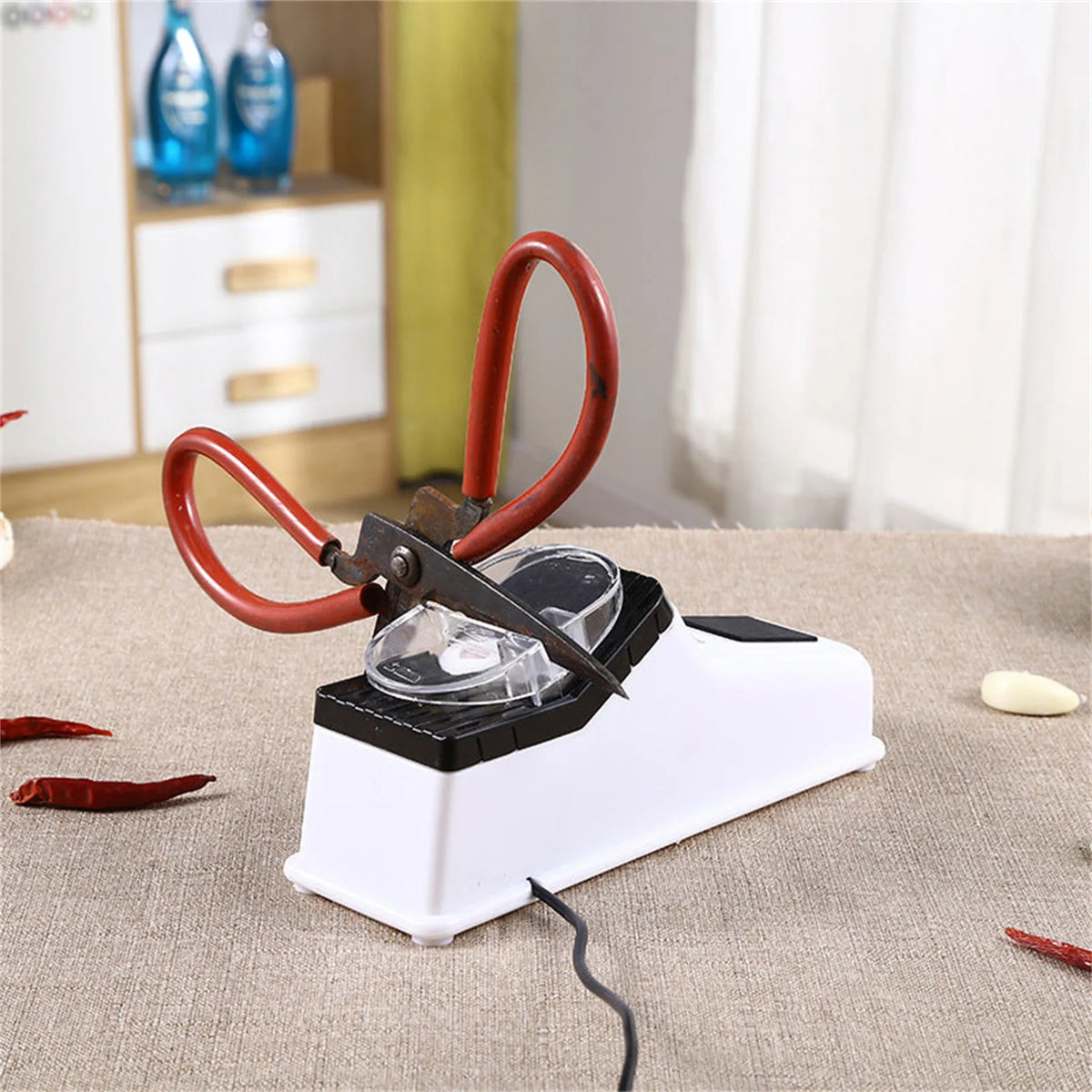 A red electric knife sharpener with a protective cover rests on a beige cloth.
