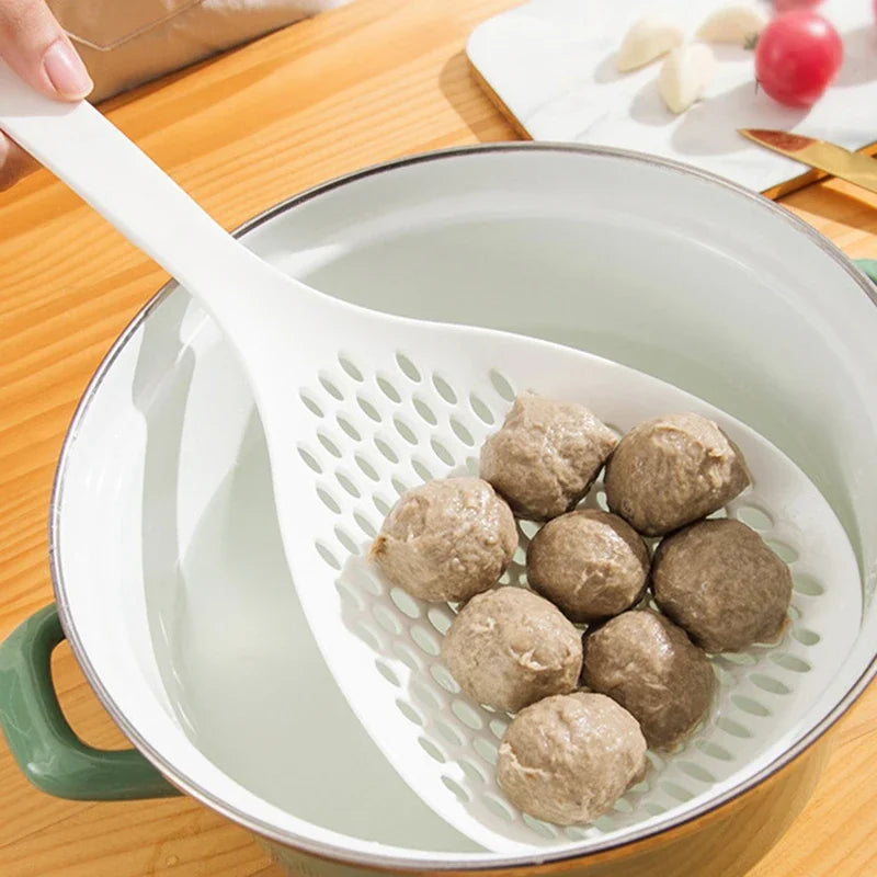 A white long-handled kitchen strainer spoon holds small brown food balls in a round metal colander.