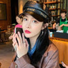 A woman wearing a black PU leather beret hat and a brown leather jacket is taking a selfie.