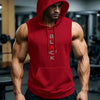 A muscular man wearing a red hooded tank top stands in a gym setting.