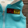 A light blue fleece pajama top with a zipper and a black and yellow embroidered patch featuring a bear face.