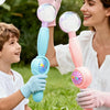 A parent and child interact by blowing bubbles using a pink smoke bubble wand with LED lights in a grassy outdoor setting.