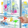 A hand is interacting with a set of ten colorful stretchy spider web sticky wall climbing toys against a blurred city backgro