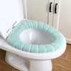 A white toilet features a light mint green soft acrylic seat cover installed around the rim.