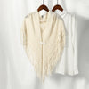 A cream knitted cotton tassel wrap shawl displayed on a hanger next to a white shirt.