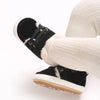 A close-up of a pair of black baby winter snow boots with white fuzzy trim and white canvas fabric.