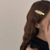 A close-up of a woman's hair featuring two gold matte resin side clips used to secure long brown hair.