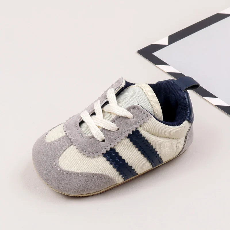 A pair of baby first walker shoes featuring light gray and cream colors with navy blue stripes.
