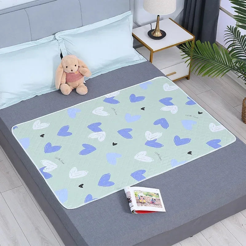 A light blue waterproof baby mattress protector featuring a cute cartoon design on a gray bed.