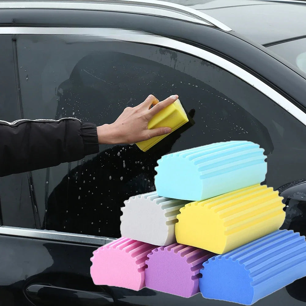 Una mano sostiene varias esponjas de limpieza PVA de colores brillantes contra una ventana oscura de coche.