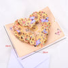 A wreath made of dried flowers and butterflies is displayed on a light pink card.