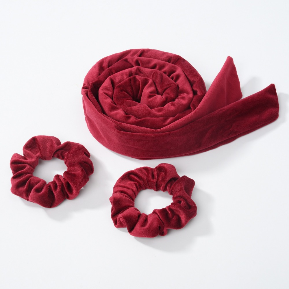 A deep red velvet heatless curling rod headband rolled into a coil and two separate fabric loops.