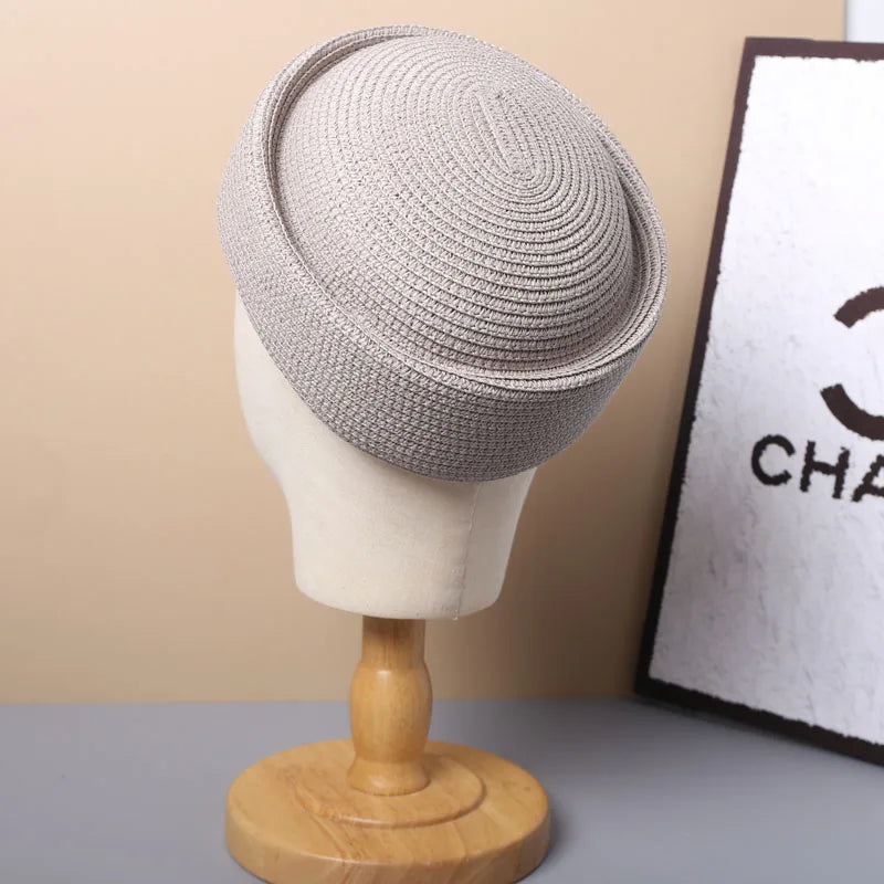 A beige straw pillbox sun hat displayed on a mannequin against a light background.
