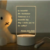 A white acrylic message board desk lamp displaying a handwritten message on a clear panel.