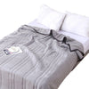 A gray quilted throw blanket is folded on a white bed with white pillows.