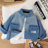 A blue and white striped denim jacket for kids lying on a white cloth next to a stack of books.