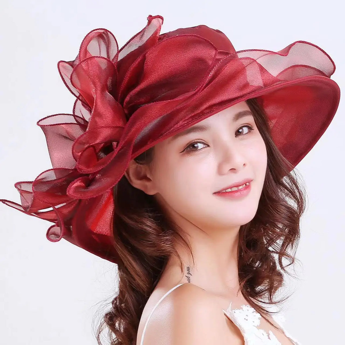 A close-up of a woman wearing a wide brim organza sun hat with ruffled mesh in a deep red color.