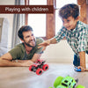A boy is playing with a red pull-back stunt SUV toy car on a wooden table.
