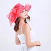 A woman wearing a pink ruffled organza sun hat and a white dress, looking upwards.