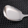 A silver stainless steel serving spoon with a long handle resting on a black textured surface.