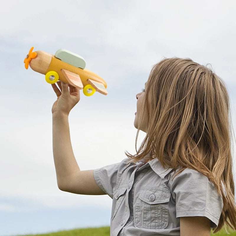 A young girl is holding a wooden number train set with an orange body and green top against a light sky.