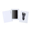 A white frame holds a black handprint and footprint keepsake on a white card.