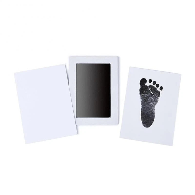 A white frame holds a black handprint and footprint keepsake on a white card.