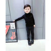 A young boy wearing a black knit turtleneck sweater and dark pants standing in front of a framed sign.