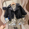 A black faux leather zipper jacket displayed on a hanger, worn over a floral patterned shirt.