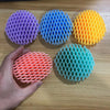 Una mano sostiene varios juguetes antiestrés de gusano 3D, coloridos y elásticos, sobre una superficie de madera.
