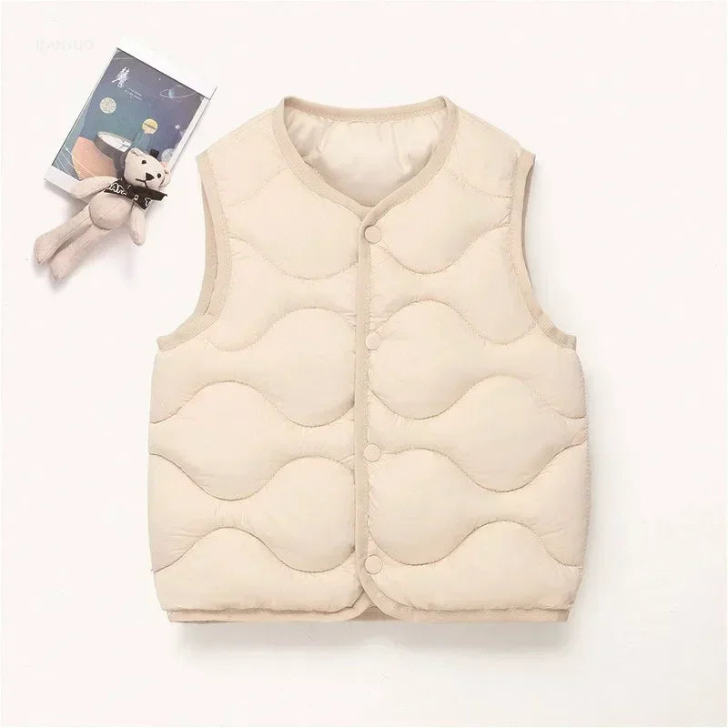 A beige quilted vest for children lying next to a small plush toy.