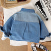 A blue denim jacket with a striped collar and front, laid on a white cloth next to a book.
