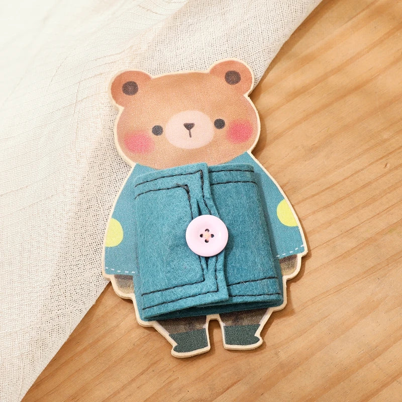 A wooden Montessori busy board featuring a bear character in a blue jacket with a pink button.