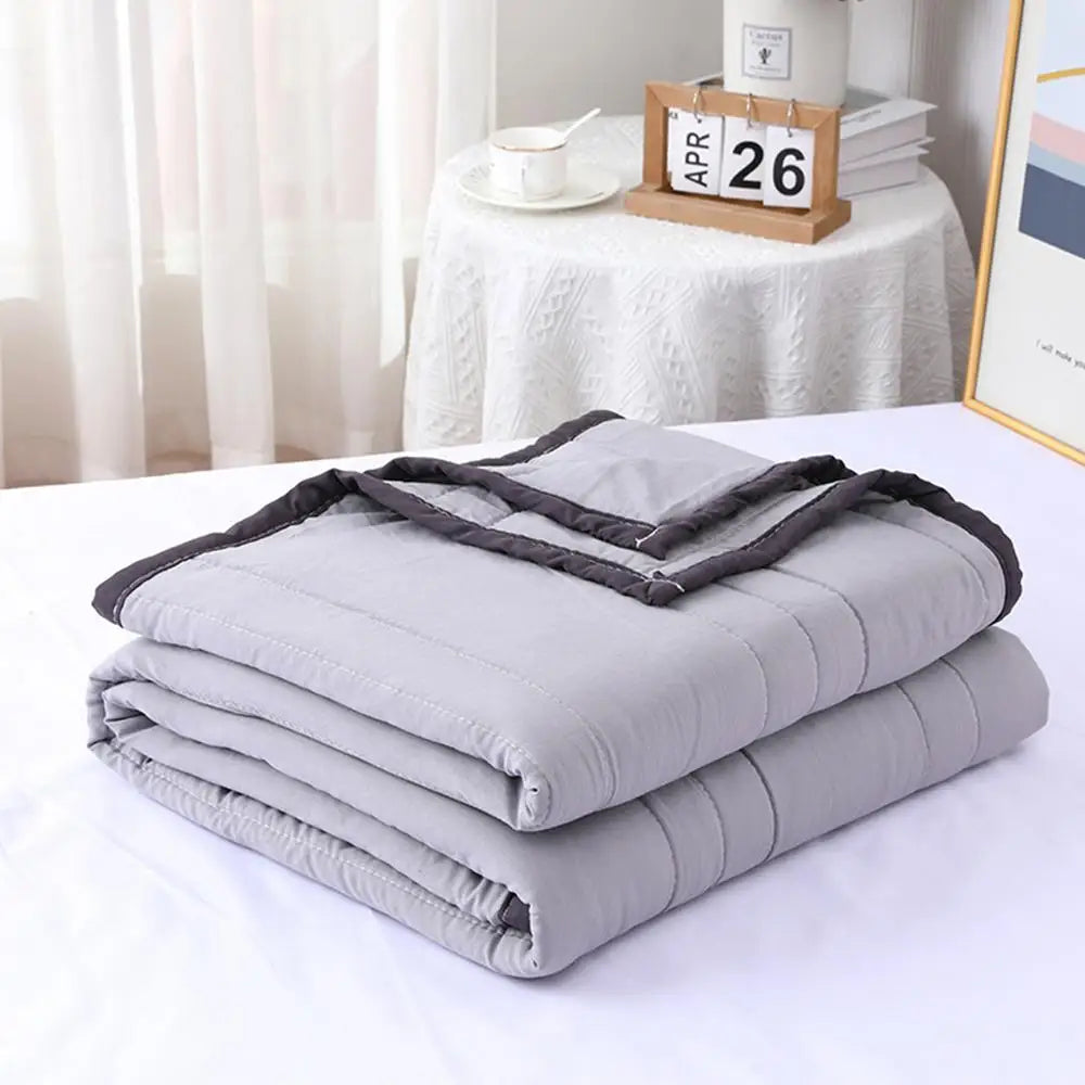 A stack of soft gray breathable cooling throw blankets folded neatly on a white surface.