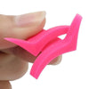 A hand holds a pink plastic winged eyeliner stencil set with curved tips.