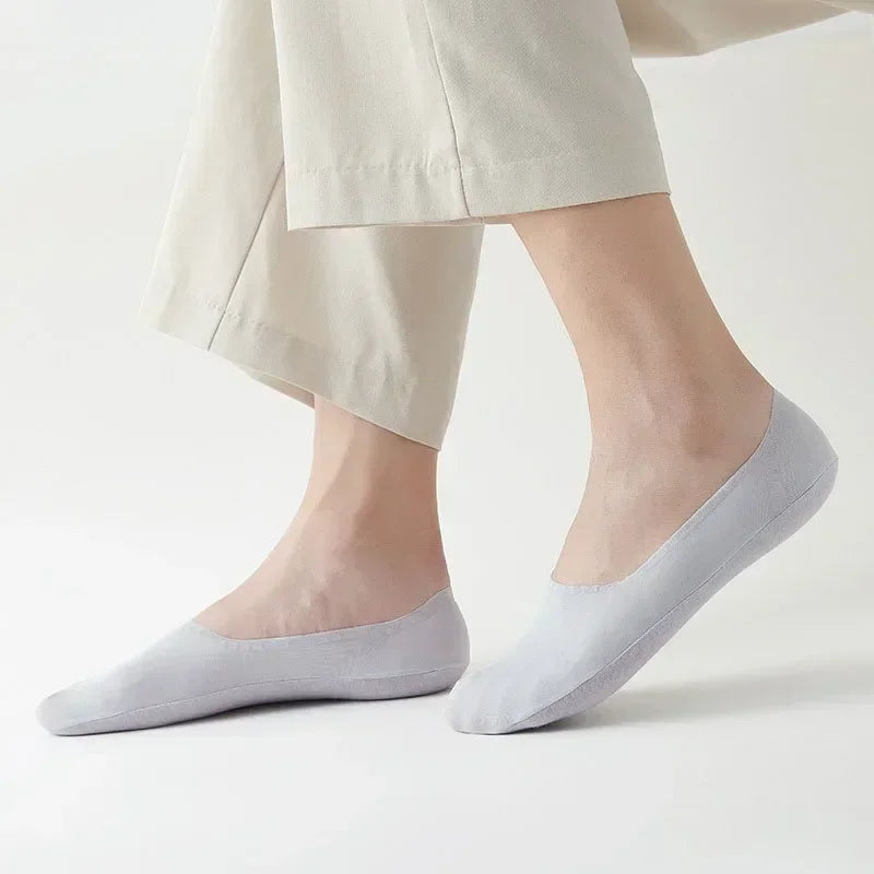 A pair of light gray silicone grip no-show socks worn on a person's foot.