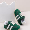A pair of green baby first walker shoes with white stripes and white laces resting on a white background.