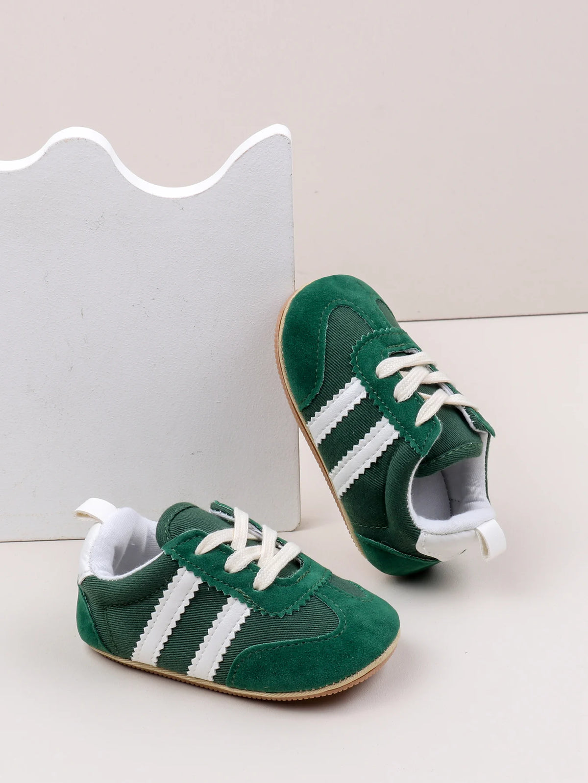 A pair of green baby first walker shoes with white stripes and white laces resting on a white background.