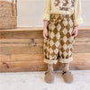 A child wearing beige long-sleeved shirt and brown diamond patterned harem pants with fuzzy boots.