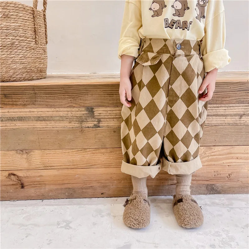 A child wearing beige long-sleeved shirt and brown diamond patterned harem pants with fuzzy boots.