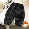 Black fleece-lined polka dot pants laid flat on a white surface next to a beige hat and a wooden basket.