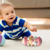 A smiling baby is interacting with a pink and yellow roller toy on a light surface.