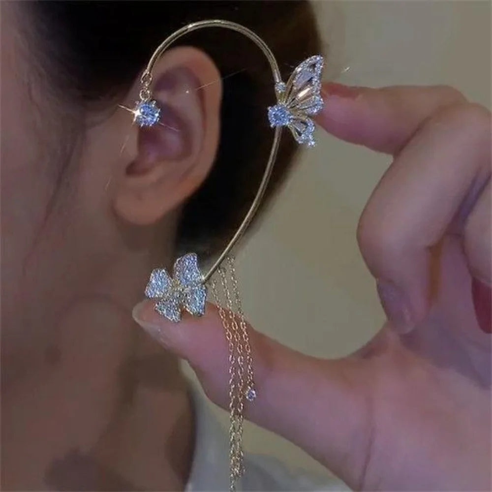 Gold ear cuff with butterfly zircon accents and a gold tassel shown being held by a hand.