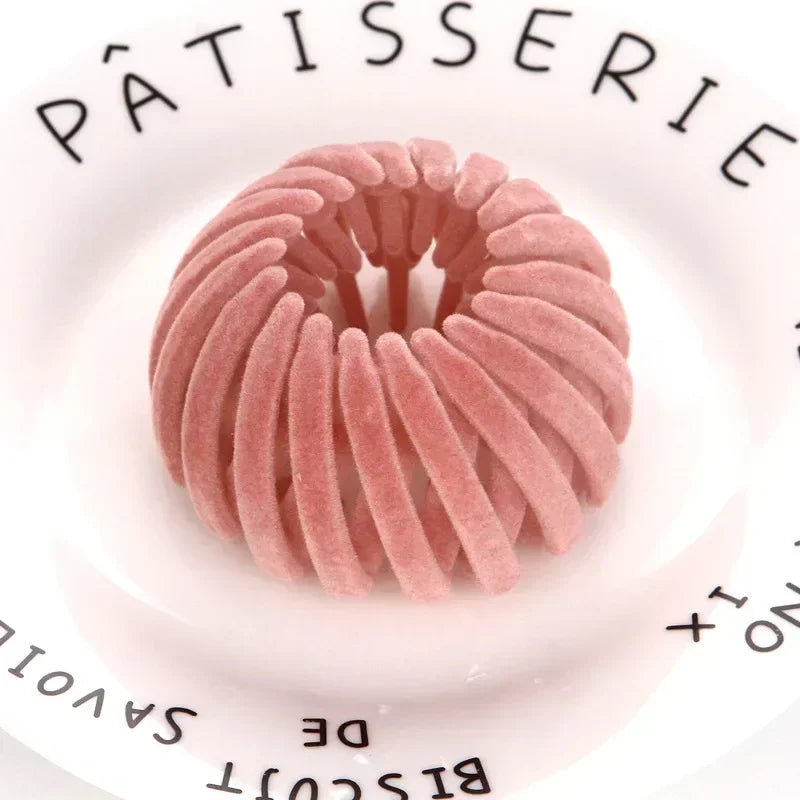 En rosa hårspenne i form av et fuglerede er vist på en hvit tallerken med tekst på kanten.