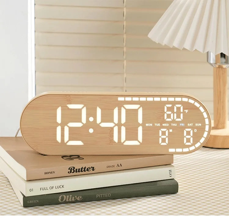 A light wood digital clock displaying 12:40, 60°F, and the day of the week, resting on a stack of books.