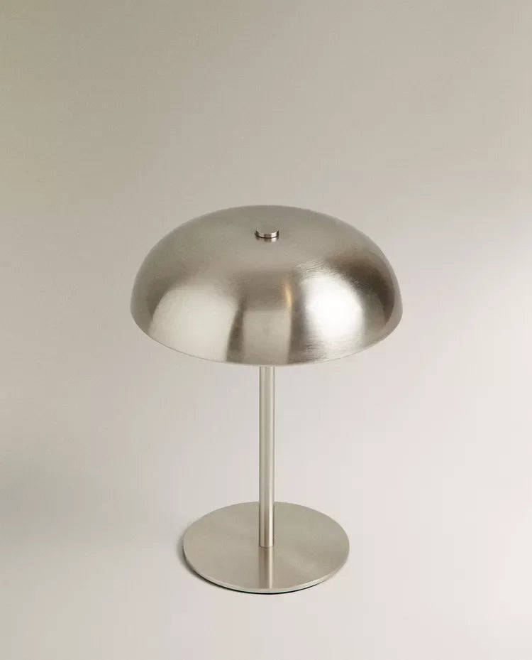 A modern, silver-toned portable touch table lamp with a dome shade and a cylindrical stand.