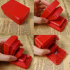 A hand holds an open red 3D-printed box with nested layers against a background of text.